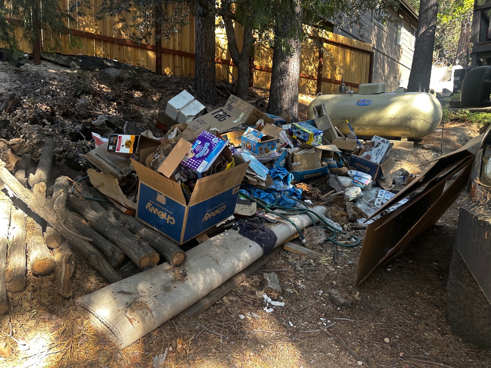 Backyard piled with cardboard boxes, trash, and debris before a Royce Professional Services cleanup